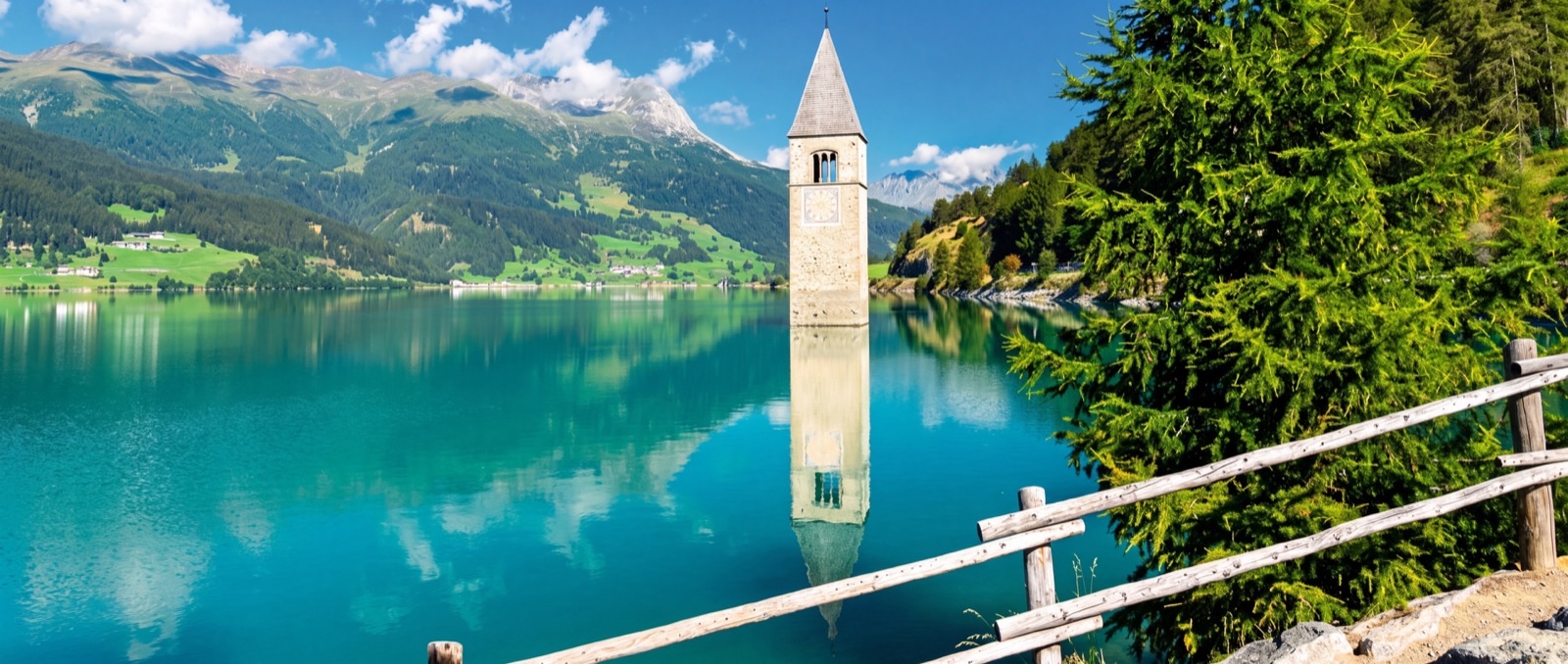 Der Kirchturm von Alt-Graun im türkisen Reschensee, dahinter die Berge des Vinschgaus